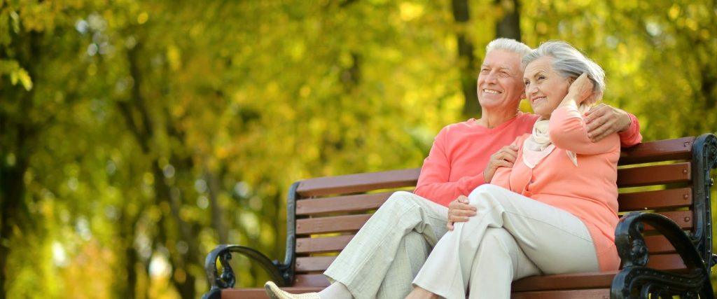 Happy Elderly Couple Sitting On Bench In Autumn Park Edited 1